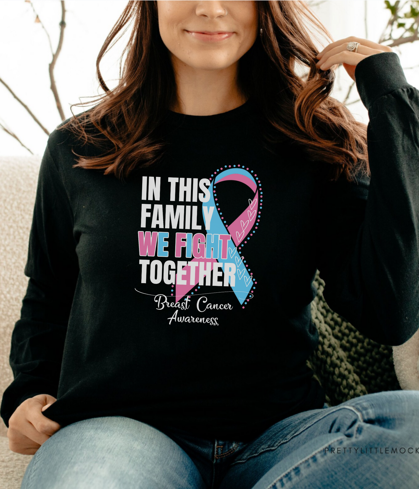 a woman sitting on a couch wearing a black shirt with a pink and blue ribbon