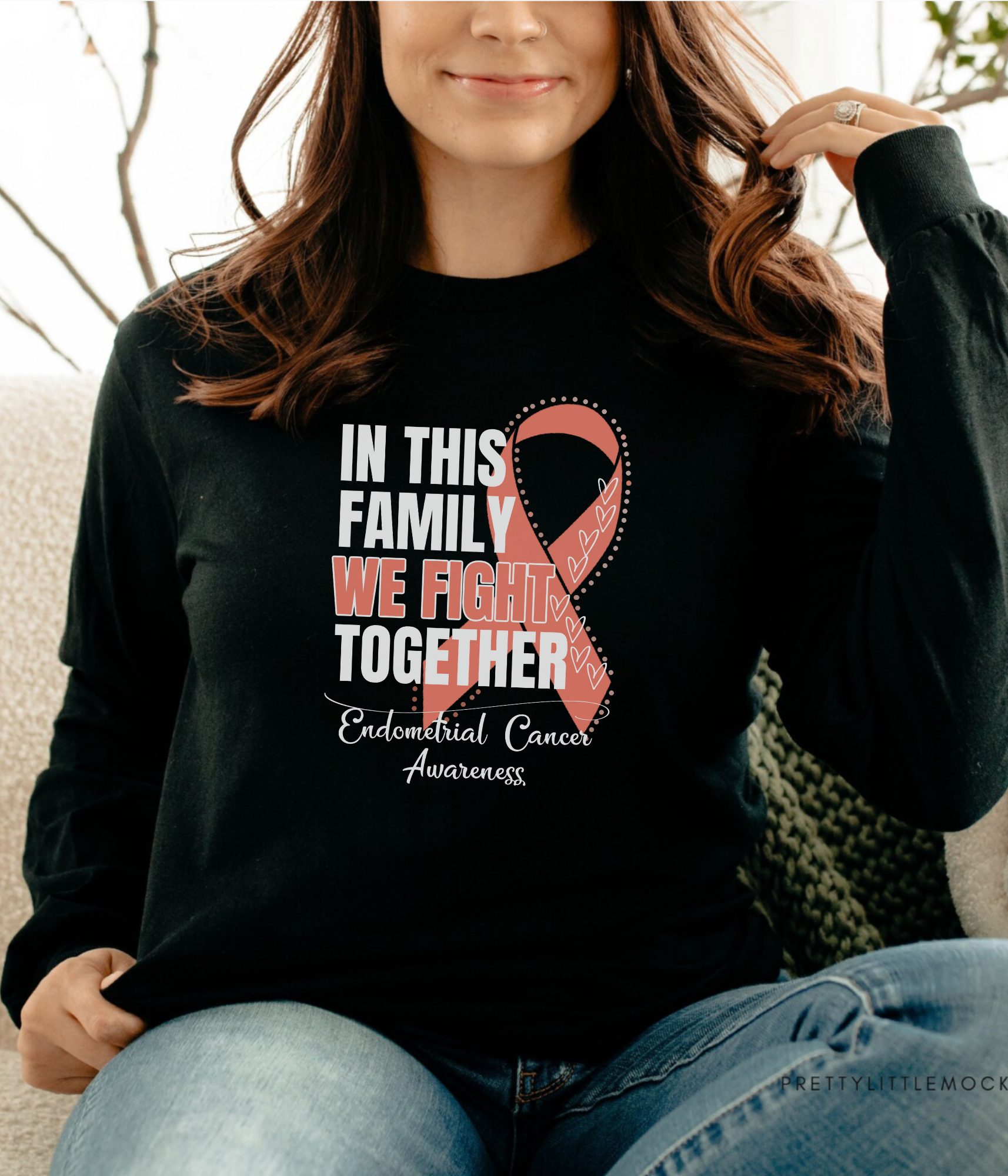 a woman sitting on a couch wearing a black shirt with a pink ribbon on it