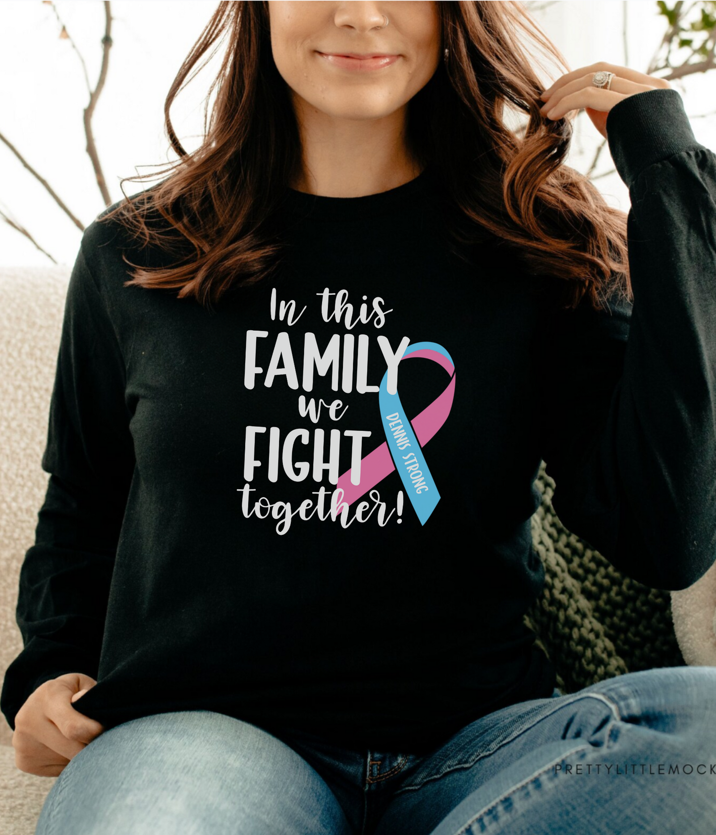 a woman sitting on a couch wearing a black shirt with a pink and blue ribbon