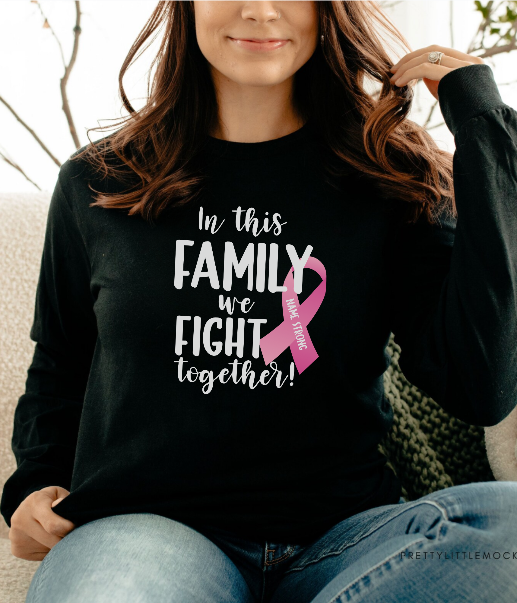 a woman sitting on a couch wearing a black shirt with a pink ribbon