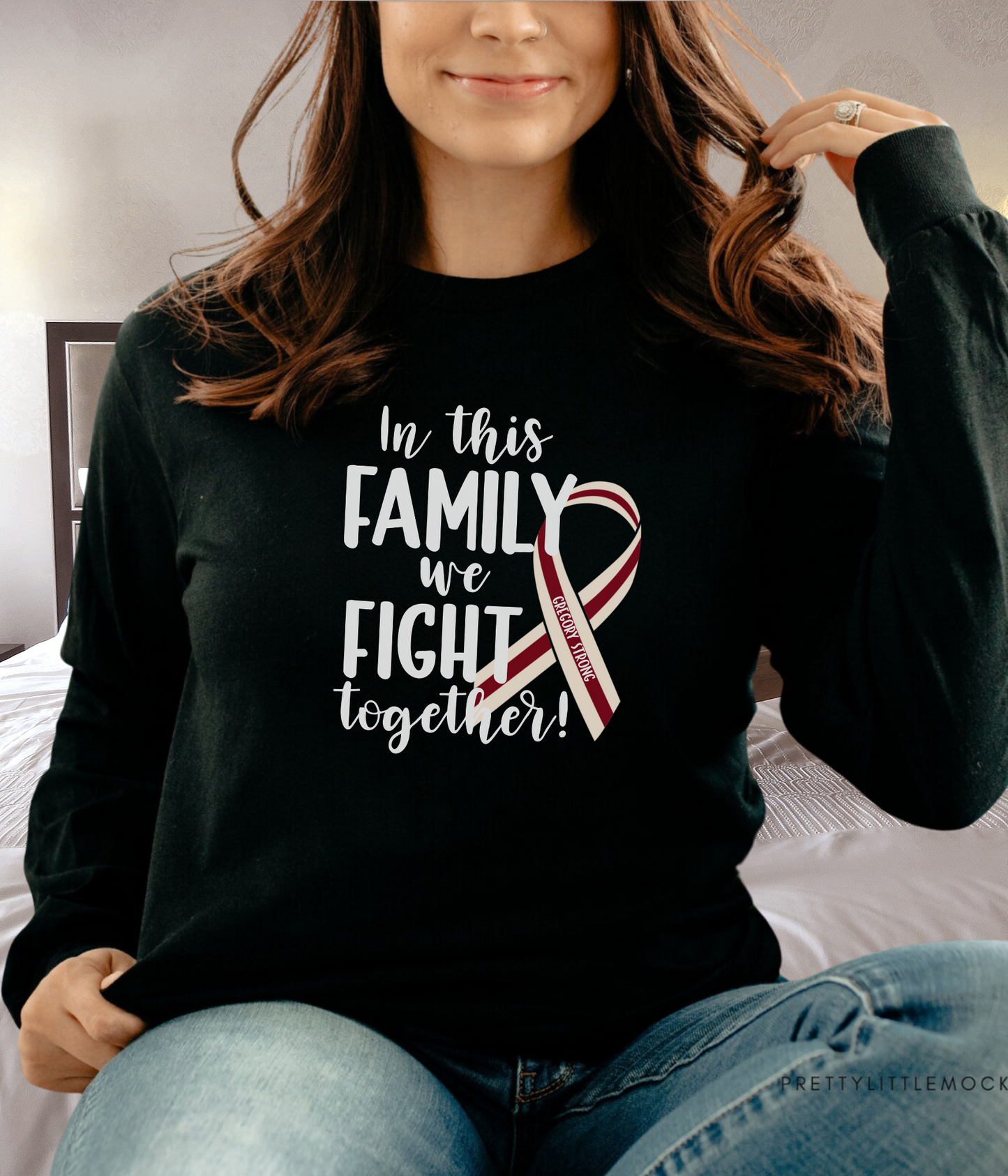 a woman sitting on a bed wearing a black shirt with a red and white ribbon