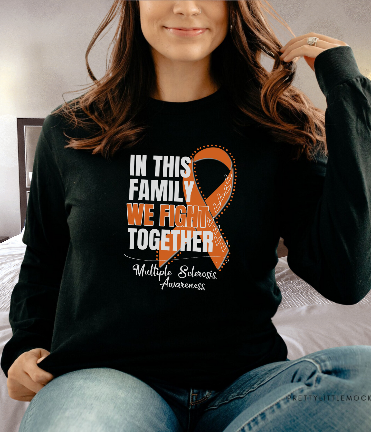 a woman sitting on a bed wearing a black shirt with an orange ribbon